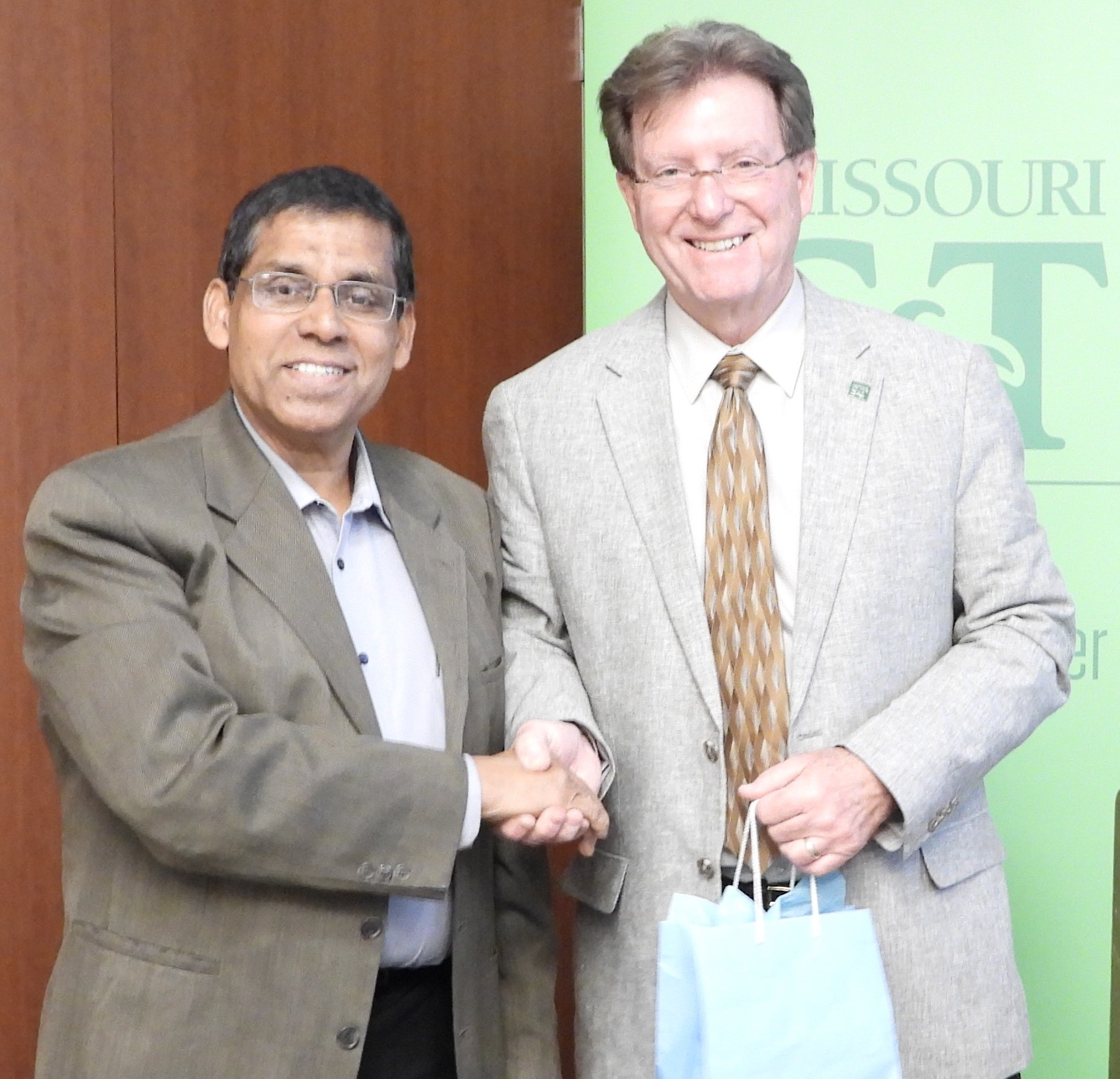 Guest speaker, Timothy Faley, holding a gift bag, shaking hands, and smiling with Sajal Das.